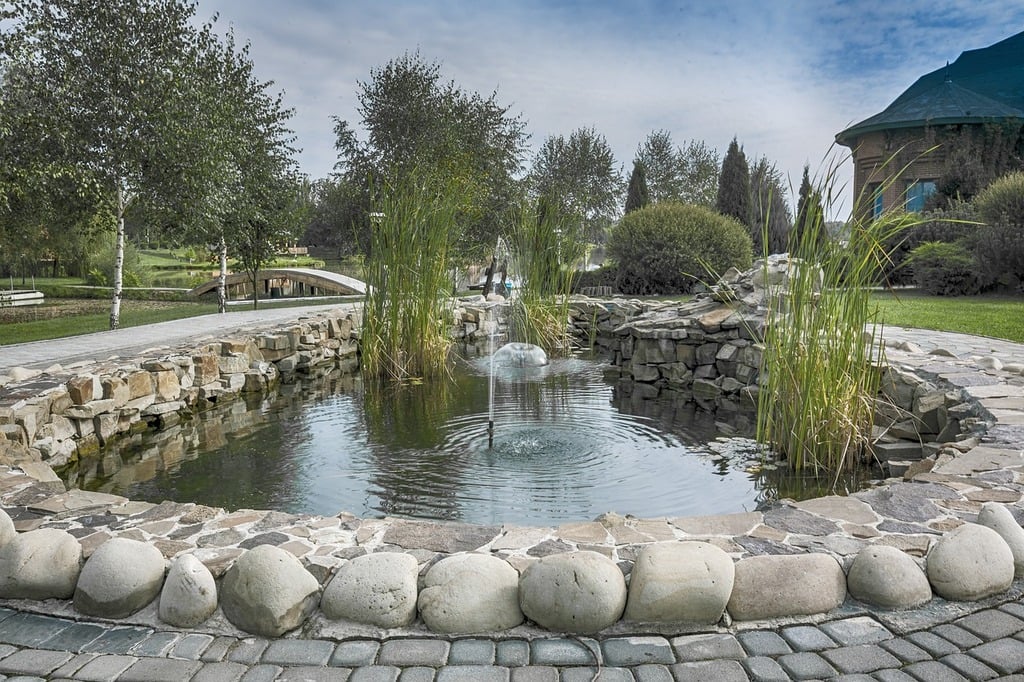 A large pond with rocks and plants around the edge and two water fountain pipes in the middle